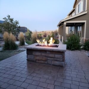 A stone fire pit sits on a paved patio near a modern house