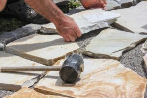 A person is laying stone slabs on gravel, using hands to position them precisely.